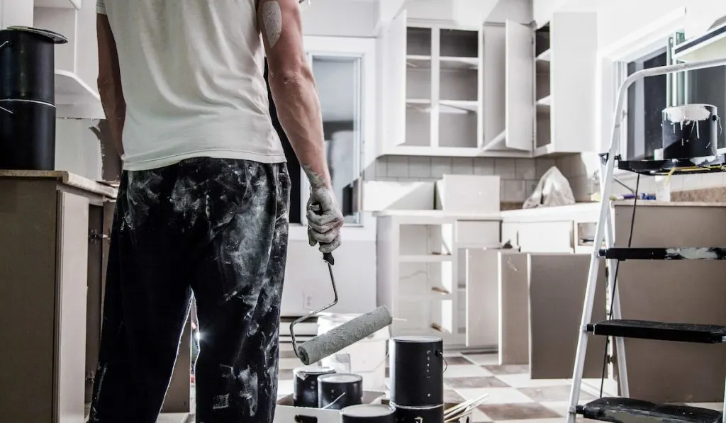 man holding paint roller doing kitchen cabinet paint job