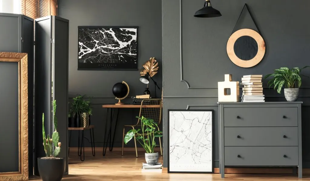 Black map on grey wall in dark living room interior with plants and poster