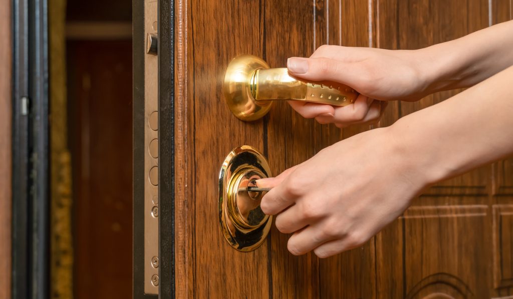 Woman's hands open a brown front door with a gold handle with a key